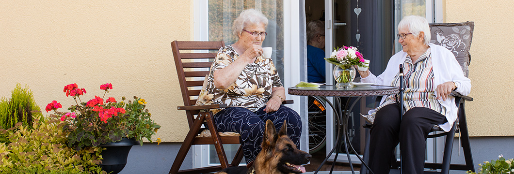 Zwei ältere Frauen sitzen auf einer Terrasse und trinken Kaffee.