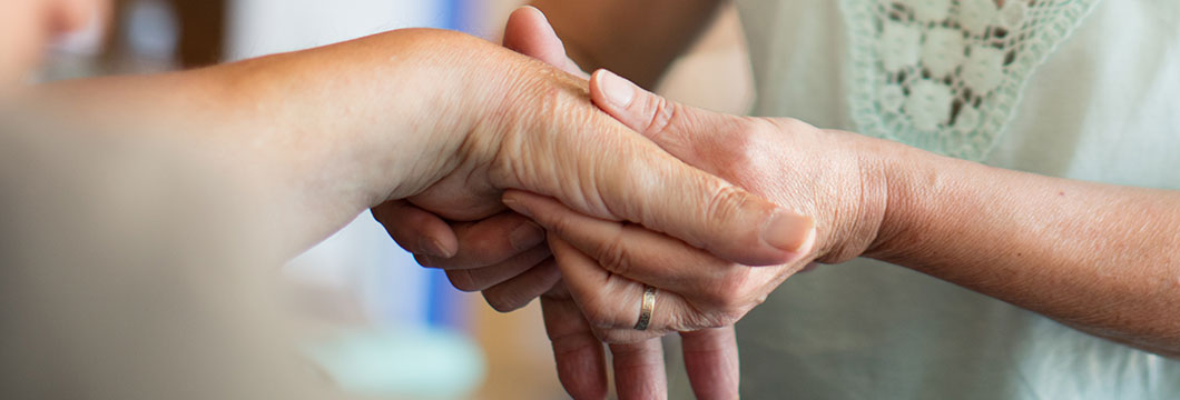 Die Hand einer Seniorin liegt in den massierenden Händen einer Pflegerin.